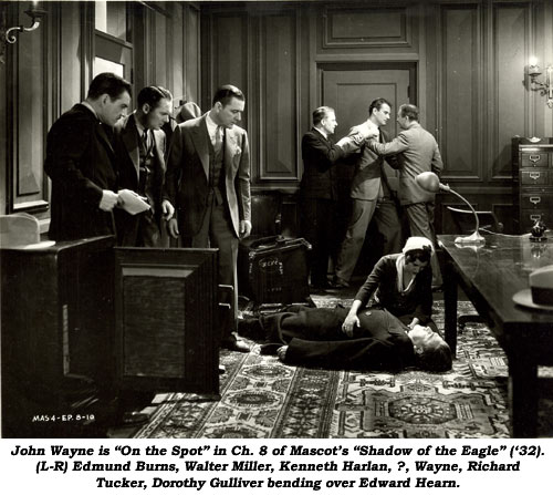 John Wayne is "on the spot" in Ch. 8 of Mascot's "Shadow of the Eagle" ('32). (L-R) Edmund Burns, Walter Miller, Kenneth Harlan, ?, Wayne, Richard Tucker, Dorothy Gulliver bending over Edward Hearn.