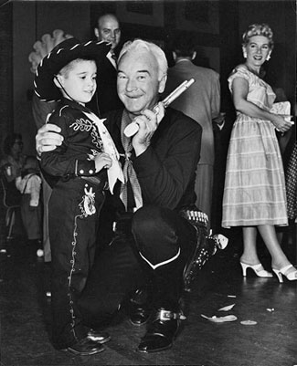 Hopalong Cassidy with a young fan. Hoppy’s wife Grace Bradley looks on. 