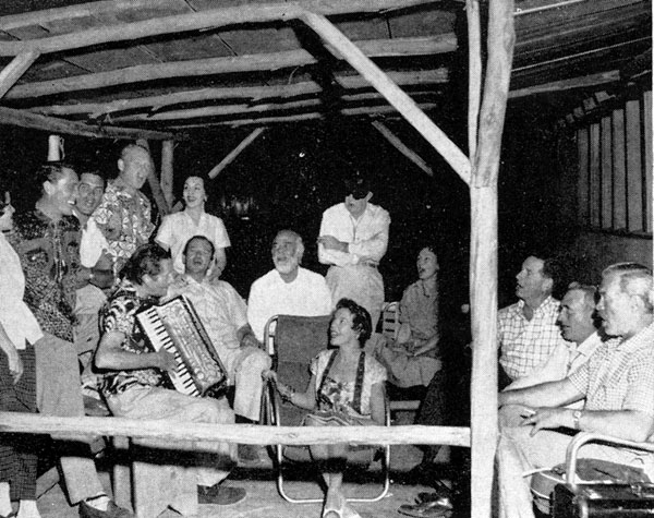 Time to relax and sing. From left, standing: Mrs. Ken Curtis, Ken Curtis, Jeffrey Hunter, Harry Carey Jr., Mrs. Wayne, John Ford (eye patch). Seated, L-R): Dan Borzage, John Wayne, Antonio Moreno, Mrs. C. V. Whitney, Dorothy Jordan, C. V. Whitney, Winton Hoch, Ward Bond.