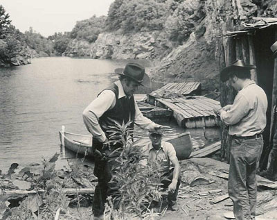 Sunset Carson and crew members prepare for the blowing up of the hideout shack scene from “Marshal of Windy Hollow” in the two photos above. In the first photo are Sunset, cameraman Darrell Cathcart and Jerry Whittington. In the second photo are an unknown lady, Sunset and Jerry Whittington.