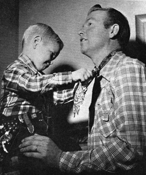 Three and a half year old Rex Allen Jr. makes an effort to tie his Dad’s neckerchief.