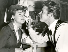 Roger Moore helps to touch up Kathleen Crowley’s make-up as they prepare for a scene on “Maverick: A Bullet for the Teacher”.