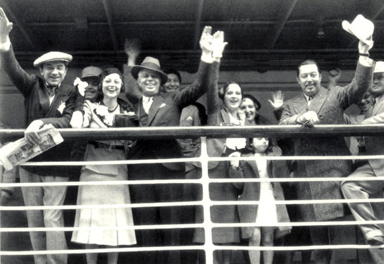 Western star Hoot Gibson prepares to sail to Hawaii with wife Sally Eilers for her role in the Charlie Chan mystery “The Black Camel” (‘31). Also in the cast are Bela Lugosi (left) and ‘Chan’ Warner Oland (waving his hat). Director Hamilton MacFadden leans on the railing beside Oland.